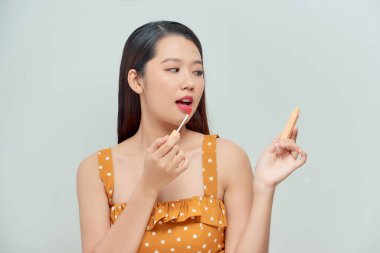 Mükemmel pürüzsüz ciltli güzel bir kadın dolgun dudaklara dudak parlatıcısı sürüyor.