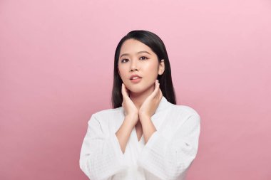 Beyaz bornoz giymiş güzel genç bir kadın yüzüne dokunuyor ve gülümsüyor.