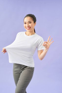 Beyaz tişörtlü, diyet sonuçlarını mor arka planda gösteren hayret verici genç kadın. 