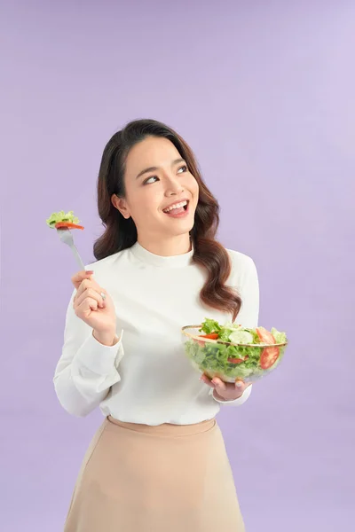 紫色の背景にボウルから新鮮なサラダを食べる幸せな遊び心のある女の子の肖像画 — ストック写真