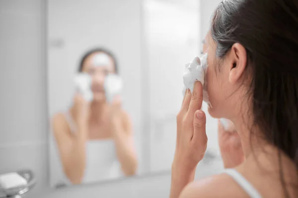 Woman happy cleanses the skin with foam on sink.