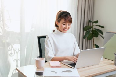 Evde bilgisayarla çalışan neşeli Asyalı kadın. 