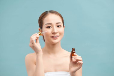 Genç bir kadının portresi menekşe arka planda yüzüne serum uyguluyor.