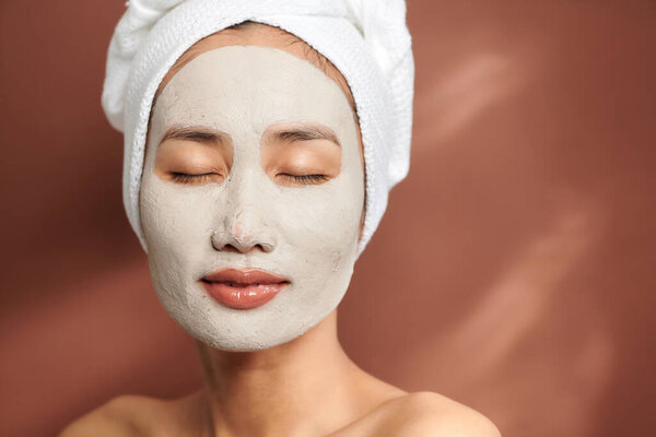 Portrait of young Asian wearing clay mask over brown background.