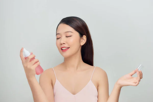 Beautiful woman applying spray water treatment on face