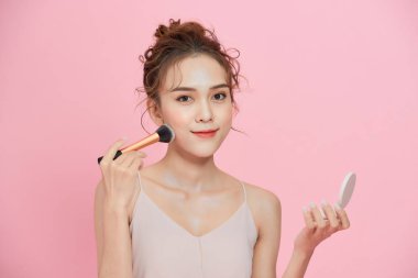 Genç ve güzel Asyalı kadın makyajını yapıyor, aynaya bakıyor.