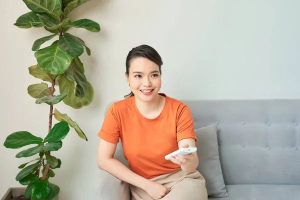 Young woman switching on air conditioner at home