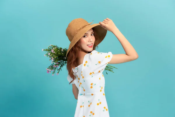 夏のドレスと麦藁帽子を身に着けている美しい若いアジアの女性は 花の花束でポーズをとって 青の背景に隔離された立って — ストック写真