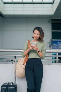 Güzel Asyalı iş kadını akıllı telefonu kullanarak uçağını kontrol ediyor ya da havaalanında bavullarıyla internet üzerinden kayıt yaptırıyor. Hava yolculuğu.