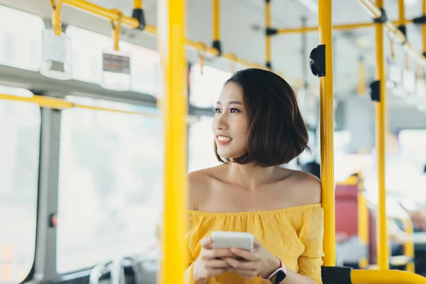 Young Asian attractive woman standing on the bus and using phone.
