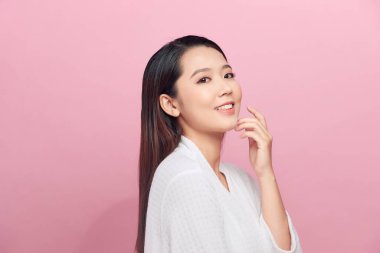 Beyaz bornoz giymiş güzel genç bir kadın yüzüne dokunuyor ve gülümsüyor.