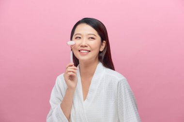 Güzel Asyalı kadın yüzüne masaj yapmak için yeşim taşı kullanıyor.