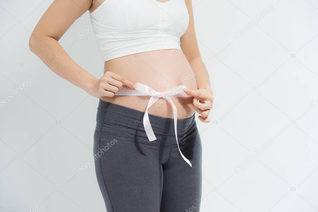Close-up pregnant woman belly with tying pink ribbon.
