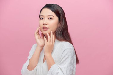 Güzel Asyalı genç bir kadın yumuşak yanak gülümsemesine dokunuyor. Temiz ve taze tenli. Mutluluk ve neşe dolu.