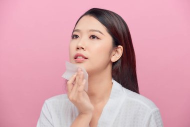 Doğal makyajlı, yağ emici çarşaf kullanan güzel mutlu Asyalı kız modelinin yakın çekimi.