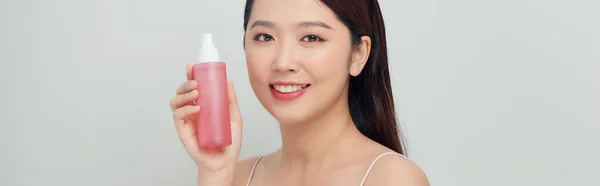 白地に化粧水の入ったピンクの瓶を持つ若い女性の肖像画 — ストック写真