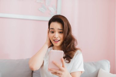 Şaşırmış bir kadın evdeki koltukta oturan telefon ekranına bakıyor.