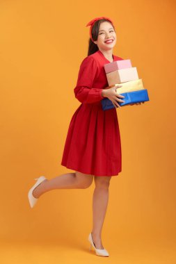 Portakal rengi arka planda izole edilmiş hediye kutuları taşıyan elbise giymiş genç bir kızın portresi.