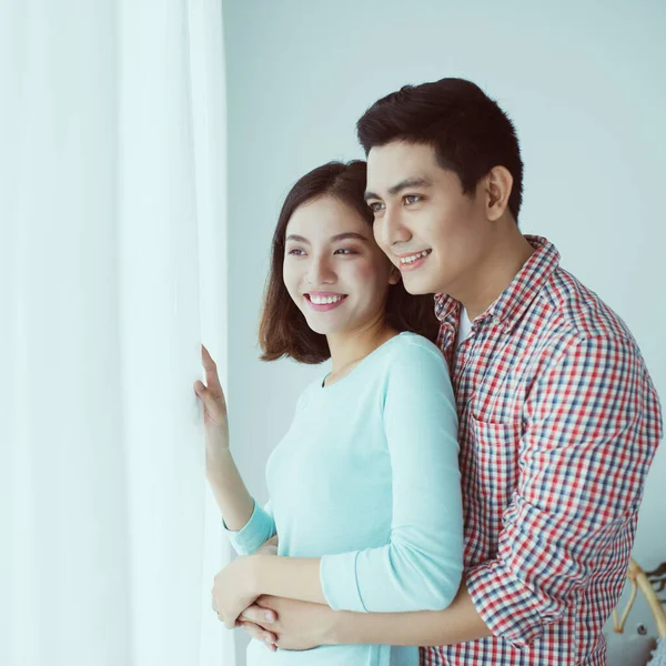 Young Asian Couple Embrace in Modern Apartment behind the window.