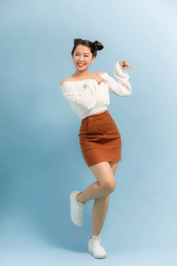 Güzel, neşeli, neşeli, güzel bacaklı, gülümseyen, mavi arka planda yaz elbisesi giyen hoş bir kadının tam boy profil fotoğrafı.