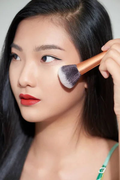 portrait of beautiful asian woman smiling while applying blush on isolated on white background