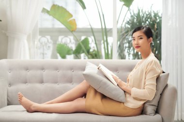 Kanepede kitap okuyan güzel bir genç kadın.