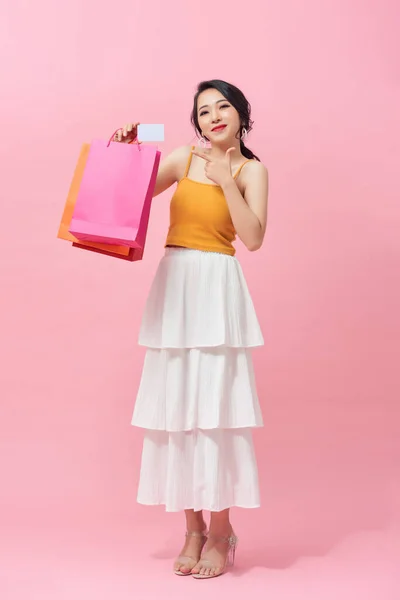 ピンクを背に立ちながらカラフルなショッピングバッグで興奮したアジアの女性の完全な長さ — ストック写真