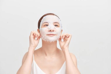 Yüzünde maske olan genç bir kız beyaz arka plandan kameraya bakıyor. Kozmetik prosedürü. Güzellik kaplıcası ve kozmetoloji.