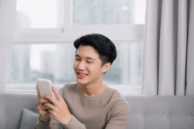 Evdeki koltukta oturmuş akıllı bir telefonla medyanın içeriğini izleyen mutlu bir adam.