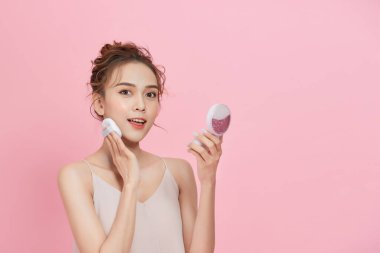 Genç ve güzel bir Aisna kadının portresi. Pembe arka planda izole edilmiş kuru toz fondöten makyajı yapıyor..