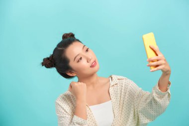 Parlak mavi arka planda izole edilmiş selfie çeken neşeli bir kadının yakın plan portresi.