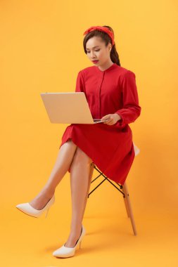 Turuncu arka planda dizüstü bilgisayar kullanan mutlu genç Asyalı kadın..