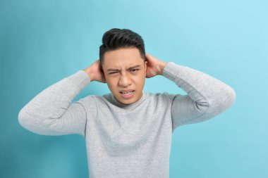 Çığlık atan bir adam ağzı açık, başını tutarak mavi arka planı izole eder, duygularla yüzleşir.
