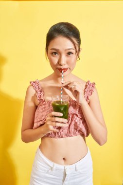 Gülümseyen genç Asyalı kadın yeşil taze sebze suyu ya da camdan meyve suyu içiyor. 
