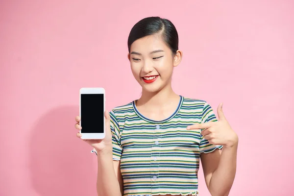 一个可爱的亚洲女孩用手指在一个空的移动屏幕上的肖像 与粉色背景隔离 — 图库照片