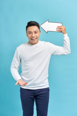 Mutlu gülümseyen genç adam, elinde büyük beyaz bir okla mavi arka planı işaret ediyor.