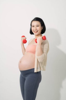 Asyalı hamile kadın egzersiz yapıyor, ayakta duruyor ve dambılları kaldırıyor, sportif hamilelik konsepti.