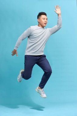 Mavi arka planda izole edilmiş komik bir adamın koşarken ya da havada zıplarken tam boy fotoğrafı.