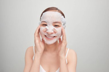 Güzel bir Asyalı kadın beyaz arka plan üzerine kozmetik maske takıyor..