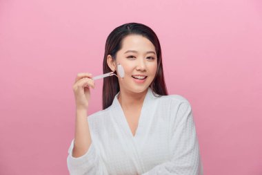 Kusursuz cildinde gül kuvars yüz silindiri kullanan sağlıklı bir kadın.