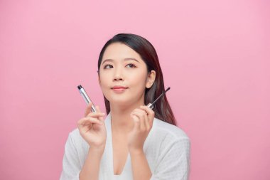 Pembe arka planda yalnız gülümseyen güzel bayan maskarayı elinde tut.