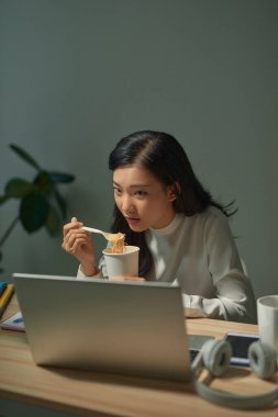 Fazla mesai yapan genç ve güzel bir bayan ödevini yapıyor ve geç saatte yemek yiyor.