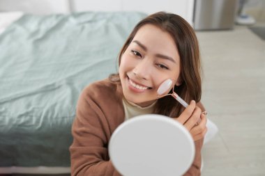 Pembe Yeşim Gül Kuvars yüz silindiri kullanan güzel bir kadın. Deri tedavisi.