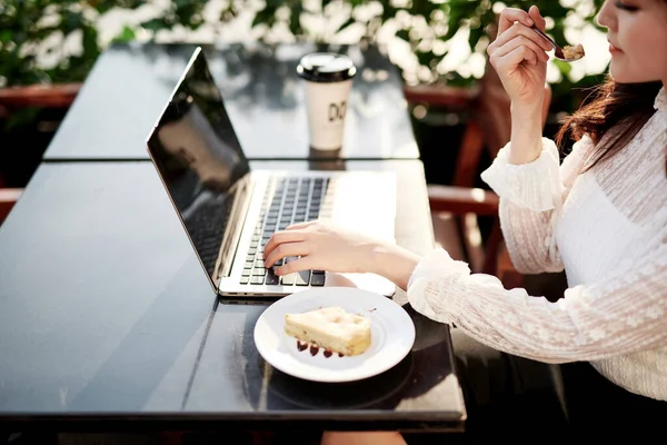 Beautiful woman eating delicious banana cake in a coffee shop. Girl in front of laptop in a coffee shop. Girl enjoying tasty cake.