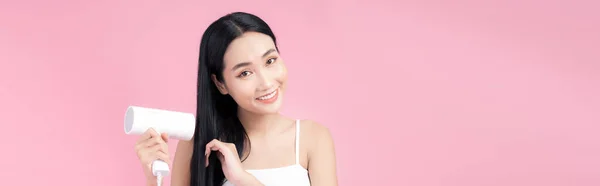 美丽的笑容 亚洲女孩与黑色长发直发使用吹风机 以粉红为背景隔离 — 图库照片