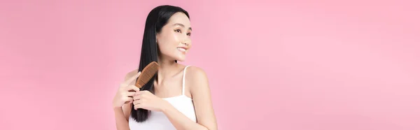 快乐的亚洲女人梳理着她美丽的黑头发 以粉红为背景隔离 — 图库照片