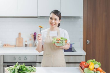 Genç kadın modern mutfakta taze salata yiyor.