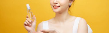 Güzel Asyalı kadın ayakta, elinde sprey şişesi, sarı arka plan