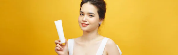 年轻的亚洲女人手里拿着一根黄色背景的白色奶油管 — 图库照片