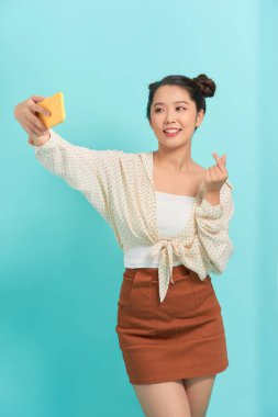 Parlak mavi arka planda izole edilmiş selfie çeken neşeli bir kadının yakın plan portresi.